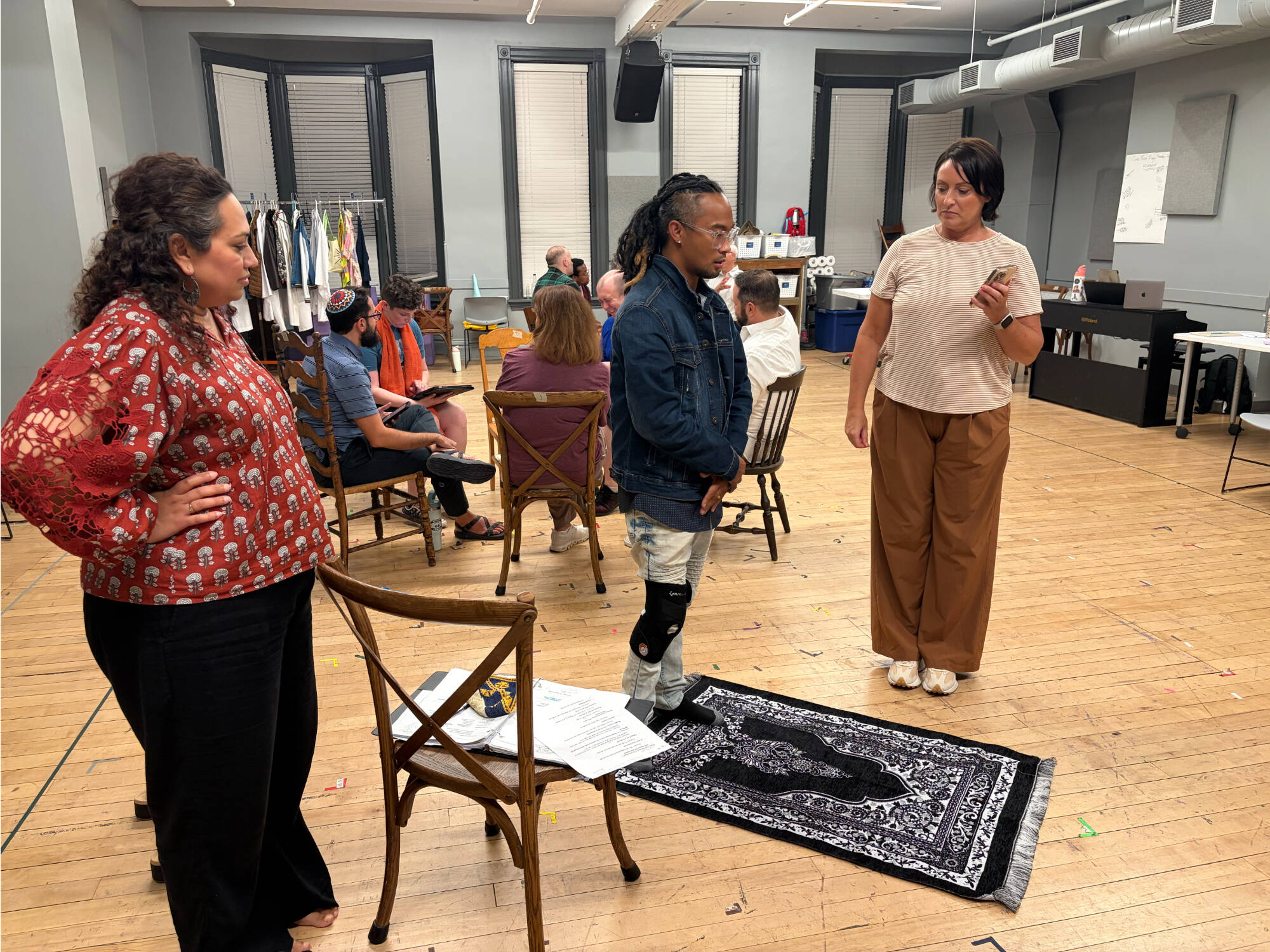 Zahabia Ahmed Usmani, left, watches a man stand in back of a rug on the floor while another person looks on